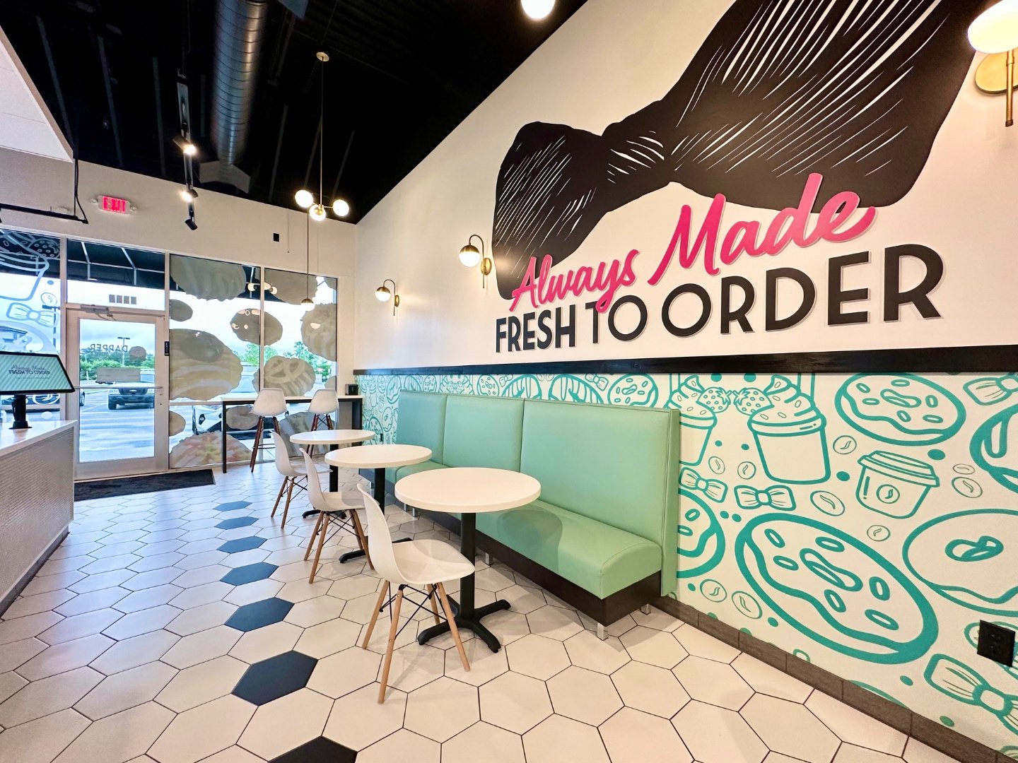 Dapper Doughnut seating area with the Always Made Fresh to Order bow-tie mural and teal booth